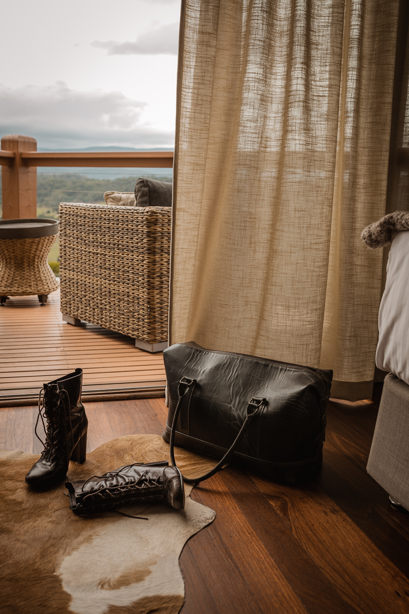 An overnight back and shoes on the floor in the foreground with curtains hinting to magnificent mountain views from the balcony. 